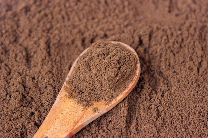 wooden spoon filled with coffee powder with a background of coffee powder