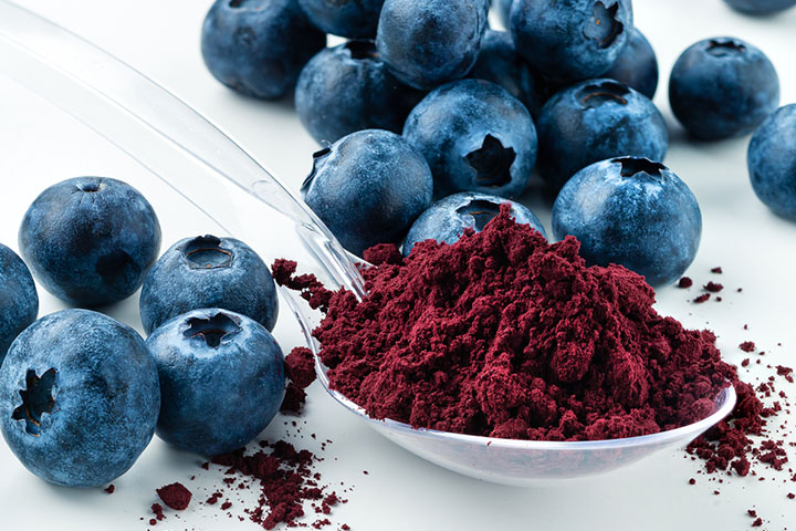 a plastic spoon filled with blueberry powder surrounded by whole blueberries