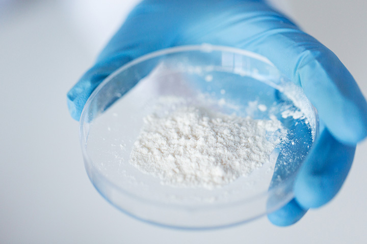 a clear container containing white powder held by a gloved hand