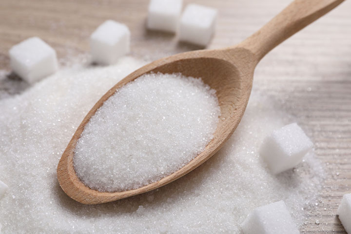 wooden spoon containing sugar on top of a heap of white sugar and sugar cubes