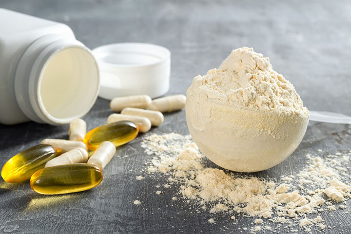 plastic scoop overflowing with powdered supplement with an open bottle and supplement capsules on the side