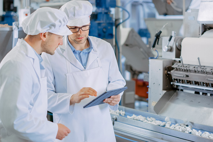 two men in lab clothing checking a tablet for quality control processes