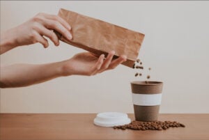 a paper bag with coffee beans poured over a paper cup